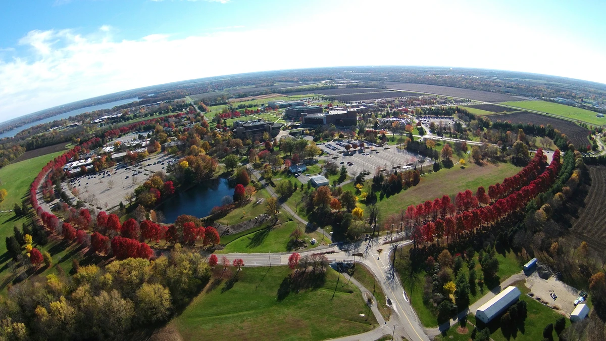 An aerial view of a sprawling landscape featuring a campus surrounded by colorful autumn trees and open fields.