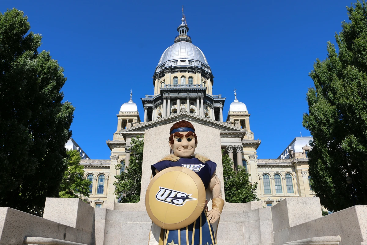 UIS mascot, Orion, with a shield stands in front of Springfield capitol building.